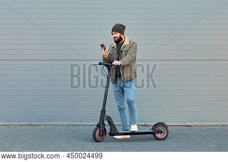 The Man With Electric Scooter Near Wall. Ecological Transportation Concept. Stylish Bearded Male Usi