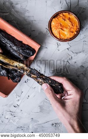high angle view of a man taking a grilled calcot, a sweet onion typical of Catalonia, Spain, before to peel it and dip it in the romesco sauce, next to him, served in an earthenware bowl