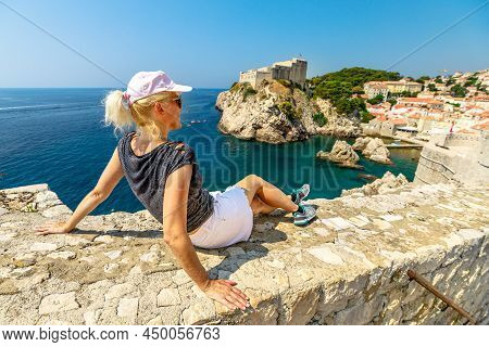 Woman On Top Walls Of Dubrovnik City Of Croatia. Looking Fort Lovrijenac Fortress, Over The West Har