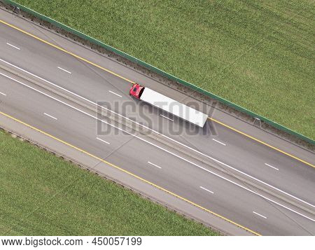 Dump Trucks Carrying Goods On The Highway. Red Truck Driving On Asphalt Road Along The Green Fields.