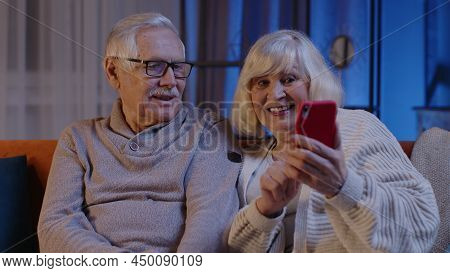 Mature Grandmother Grandfather Making Video Call Online On Mobile Phone At Home Sofa. Senior Old Cou