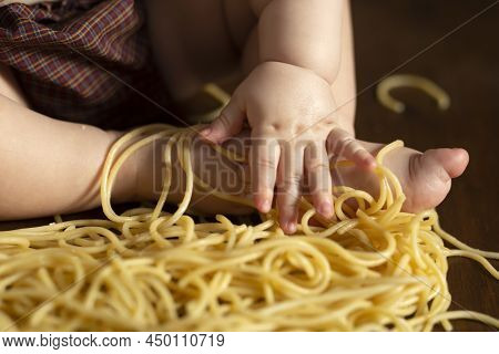 Little Chubby Kids Hand And Foot In Pasta On A Wooden Brown Background, Table. Feeding Concept. Spag