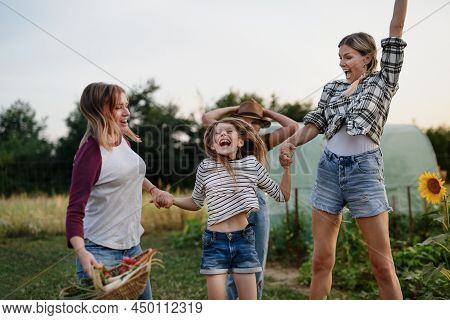 Happy Little Girl With Mother And Aunt Jumping Outdoors At Community Farm.