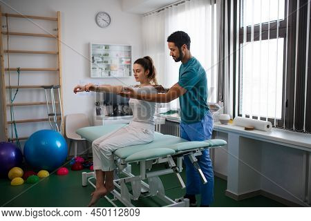 Young Male Physiotherapist Examining Young Woman Patient In A Physic Room