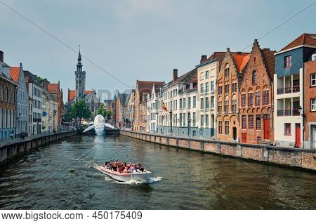 BRUGES, BELGIUM - MAY 29, 2018: Tourist boat in canal between old houses with The Bruges Whale plastic installation and The Burghers' Lodge Poortersloge tower. Brugge Bruges, Belgium