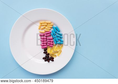 White Plate With Pills Of Nutritional Supplements In Different Bright Colors. Blue Background, Place