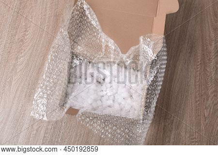 Bubble Wrap And Foam Peanuts In Cardboard Box On Wooden Table, Above View