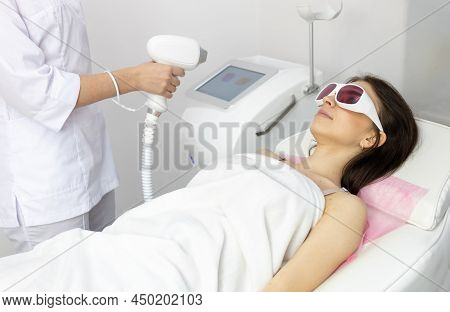 A Woman Tunes A Laser Hair Removal Machine. Girl Holding A Working Part Of The Epilator In A Modern 
