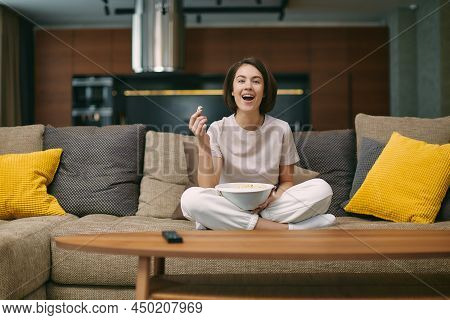 Laughing Happy Pretty Young Girl Watching Sitcom Movie Or Stand Up Comedy, Sitting On Sofa With Popc