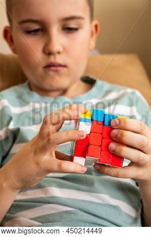 Focused Male Teenager Assembling Multicolored Pieces Of Rubiks Cube Enjoying Mind Development