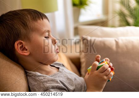 Cute Baby Boy Assembling Multicolored Rubiks Cube Solving Logical Game Lying On Couch At Home
