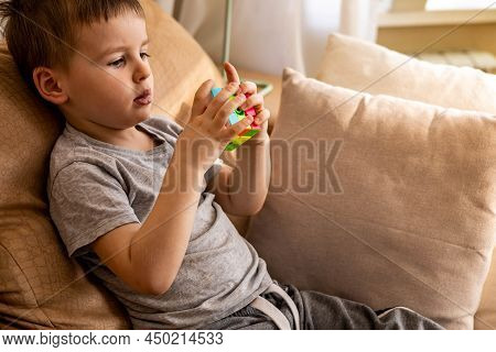 Cute Baby Boy Assembling Multicolored Rubiks Cube Solving Logical Game Lying On Couch At Home