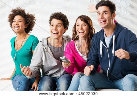 Glade gruppe af unge venner ser fjernsyn og støtte deres hold