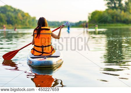 Young Woman In Orange Life Jacket On Supboard At River