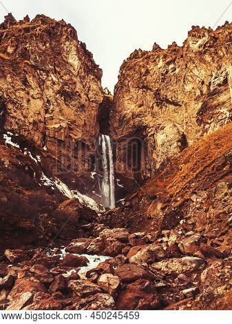 Rocky Highlands With A Waterfall Flowing Into The Gorge. Waterfall In The Mountains Of The Caucasus