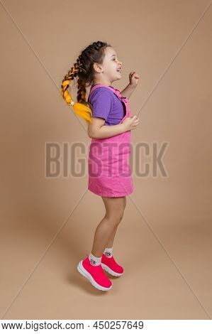 Energetic Female Kid In Process Of Jumping With Two Kanekalon Pigtails Of Yellow Color Wearing Pink 