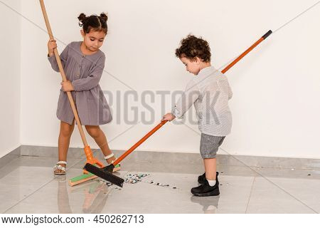 After Party. Little Curls Boy And Beautiful Girl Sweeping Confetti With Brooms. Brother And Sister C