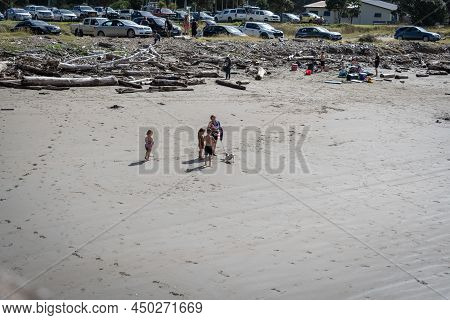 Tolaga Bay New Zealand - February 5 2022; Group Four Young People Standing On Beach With White Dog P