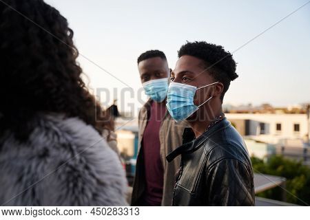 Black Male And Multi-culural Friends Chatting On A Rooftop Terrace With Masks On. City Living And Go