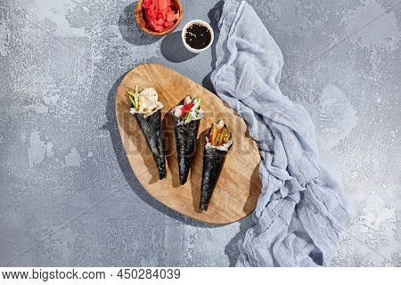 Set of temaki sushi on wooden platter in minimalistic style. Aesthetic composition with handrools on concrete background. Contemporary japanesse cuisine - temaki sushi