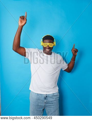 An African-american Man Is Dancing Merrily In Yellow Headphones And Stylish Glasses On An Isolated B