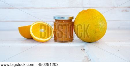 Homemade Orange Jam In A Glass Jar With Fresh Oranges On White Wood. Horizontal Background For A Swe