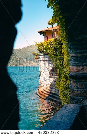Nesso, Italy - May 2021: View Of Building Covered With Vegetation On Come Lake From Crevice