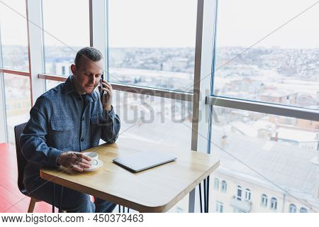 Happy Man With Coffee Calling Via Smartphone While Remote Working Laptop At Work Desk, Cheerful Free