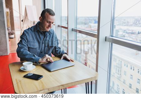 A Young Successful Businessman In A Suit Drinks Coffee And Works In A Cafe On Wireless Free Internet