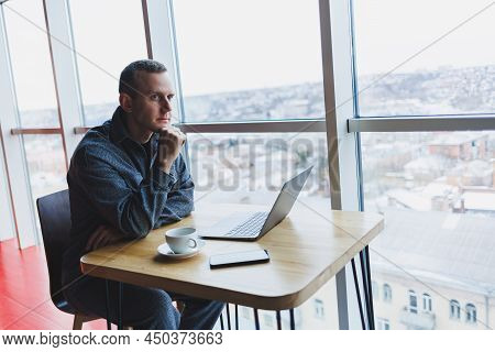 A Young Successful Businessman In A Suit Drinks Coffee And Works In A Cafe On Wireless Free Internet