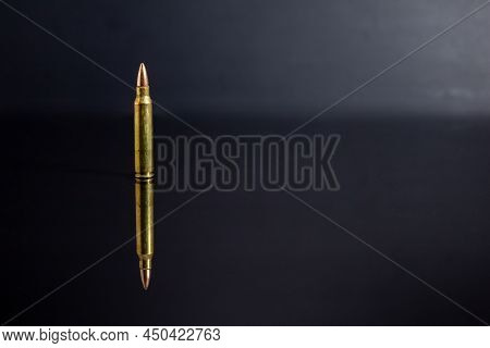 Single 5.56 Round On Black Reflective Surface And Black Background