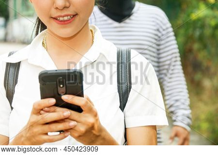 Crime Concept : Young Woman Talks On Her Smartphone Carelessly When A Dressed Man With Ill Intention