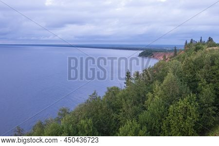 Steep Red Coast With Green Forest Over Blue Sea