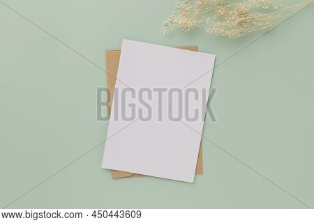 Blank Greeting Card Invitation Mockup 5x7 On Brown Envelope With Dried Flowers On Pastel Green Backg