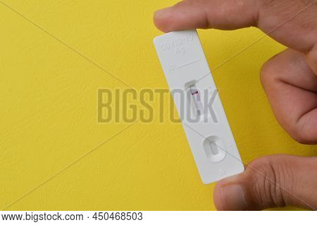 Hand Holding Covid-19 Antigen Rapid Test Isolated On A Yellow Background.