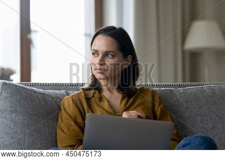 Woman Sit On Couch With Laptop Staring Aside Looking Pensive