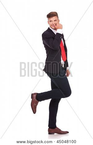 Foto de longitud completa de un joven empresario tímidamente mirando sobre su hombro con una pierna elevada y 
