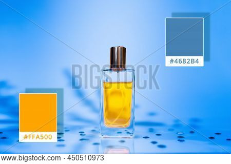 Glass Golden Perfume Bottle On A Steelblue Background With Shadows Of Plants. Samples Of Colors 4682