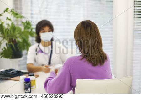 African-american Woman Doctor Wearing Face Mask Giving Cd With X-ray Image To Female Patient During 