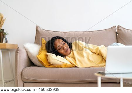 Young African-american Female Watching Movies On Laptop While Lying On Sofa In Living Room