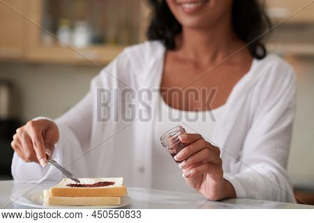 Woman Speading Homemade Jelly From Small Jar On Toast When Making Breakfast In The Morning