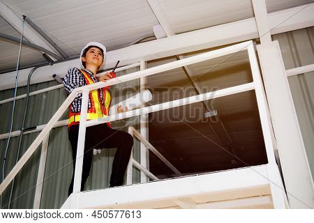 Asian Senior Female Worker In A Helmet Walks Up The Stairs Of A Fieldwork Building's Rooftop. Constr