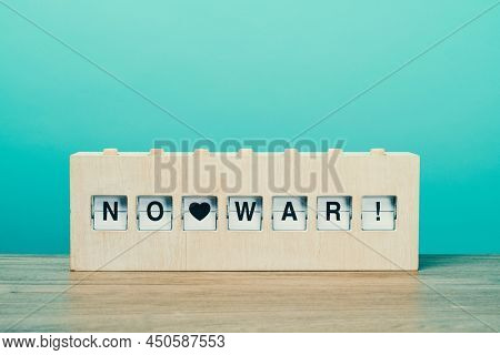 the text text no war in a rustic wooden split flap board, on a wooden surface against a blue background