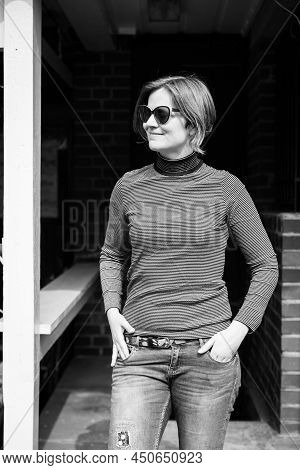 Young Thirty Year Old White Woman In A Relaxed Jeans And Sweater Outfit Posing Near An Abandonned Ca