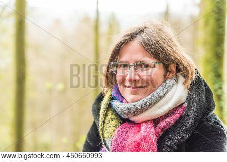 Portrait Of A Thirty Year Old White Woman With A Colorful Scarf, Glasses  And A Green Bokeh Nature B