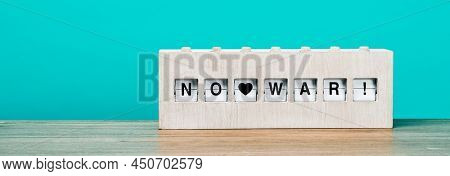 text no war written in a rustic wooden split flap display, on a wooden surface against a blue background, in a panoramic format to use as web banner or header