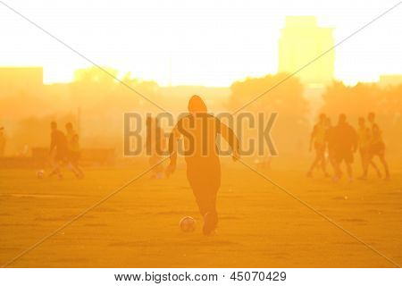 Fußballspieler läuft mit Fußball in Sonnenuntergang