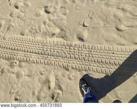 Sand And Human Foot. Beach Sand On The Sand Footprints Of A Person And A Footprint From A Car. In Th