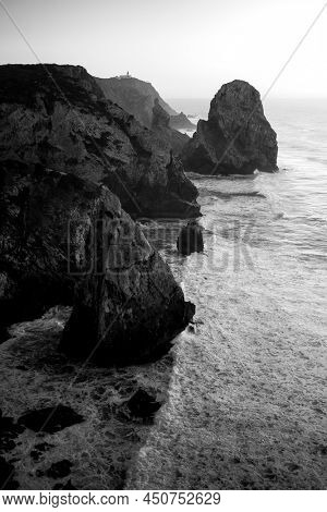 Top view of the cliffs and surf in the Atlantic Ocean at sunset, Miradouro da Praia do Caneiro, Portugal. Black and white photo.
