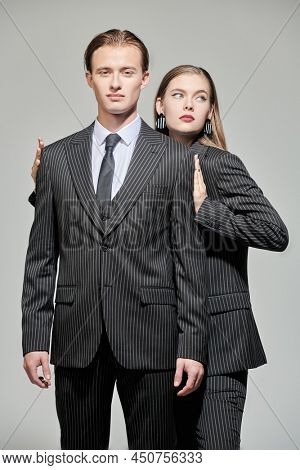 Fashion shot of stylish fashion models young man and pretty woman posing in elegant striped pantsuits on a grey studio background. Impeccable look. Men's clothing style.